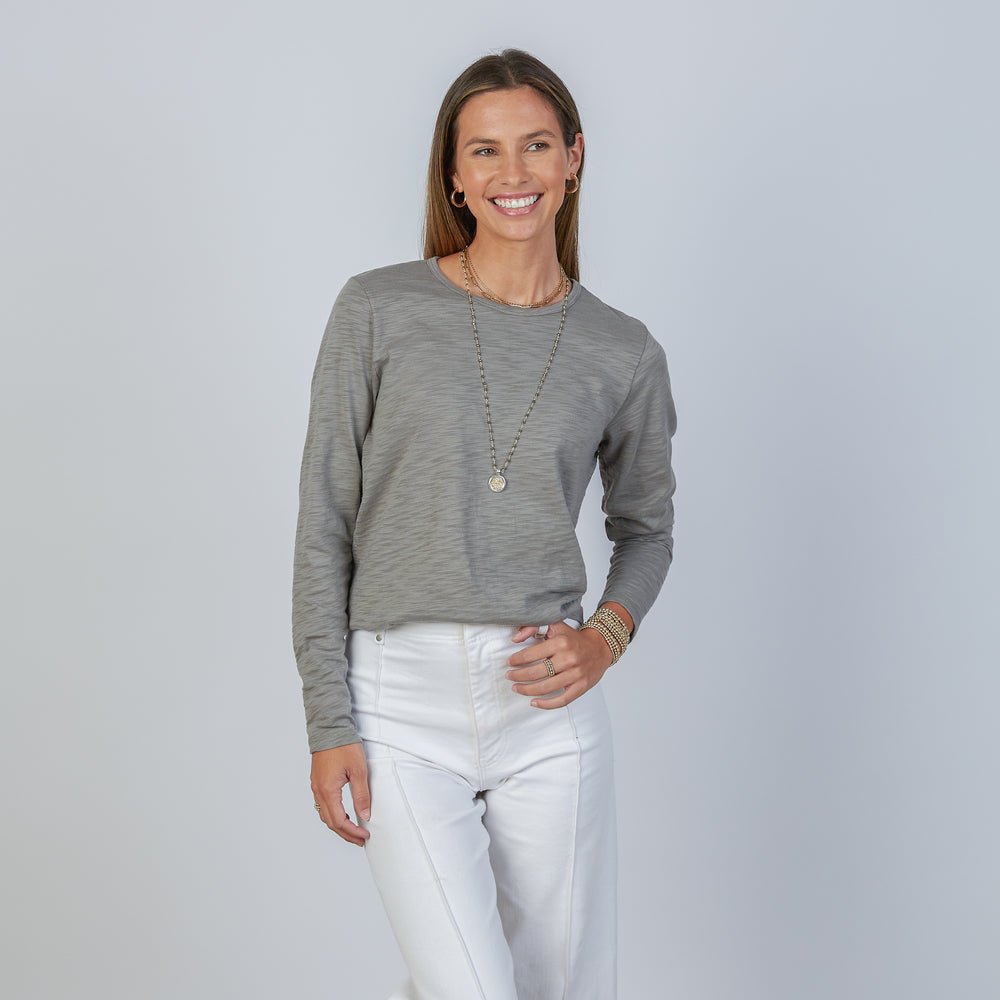 
                      
                        Woman wearing an erin gray smokey green classic long-sleeve shirt and white pants against a light gray background
                      
                    