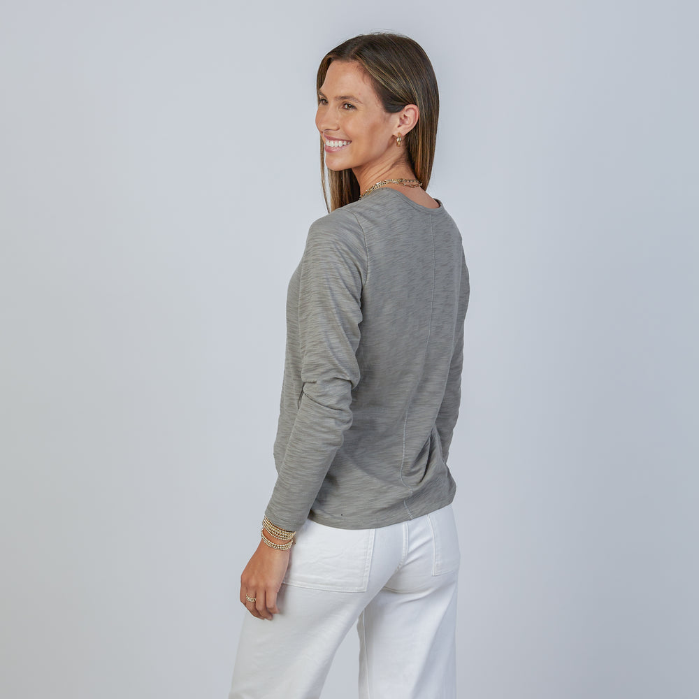 
                      
                        Woman wearing an erin gray smokey green classic long-sleeve shirt and white pants against a light gray background
                      
                    