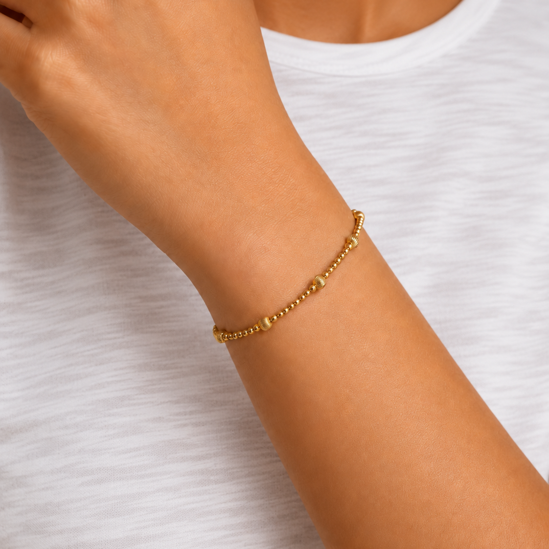 A delicate gold beaded bracelet with alternating smooth and ribbed spherical beads, displayed on a clean white background.