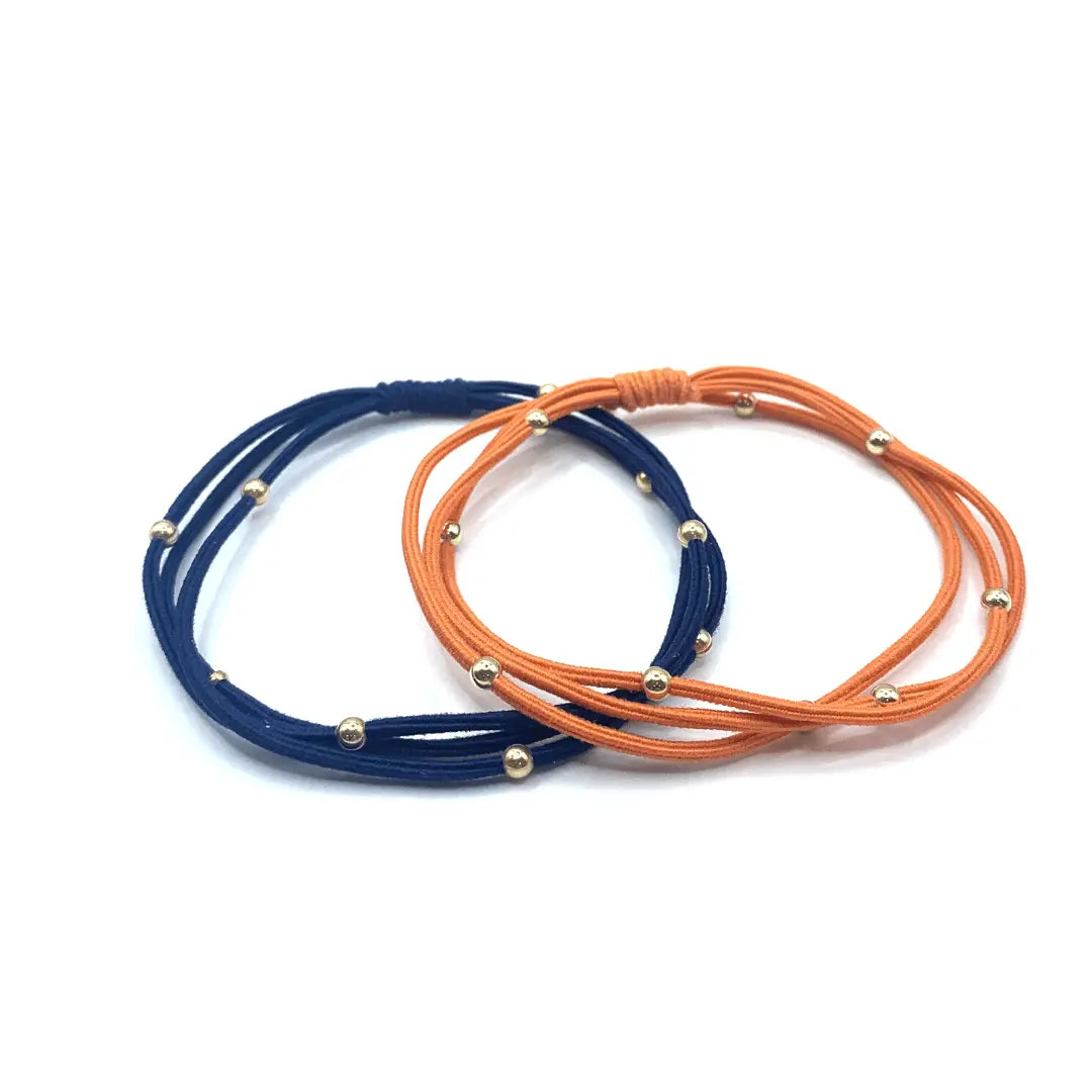 Set of erin gray 3mm gold water pony waterproof bracelet hair bands in orange and navy, shown on a white background.