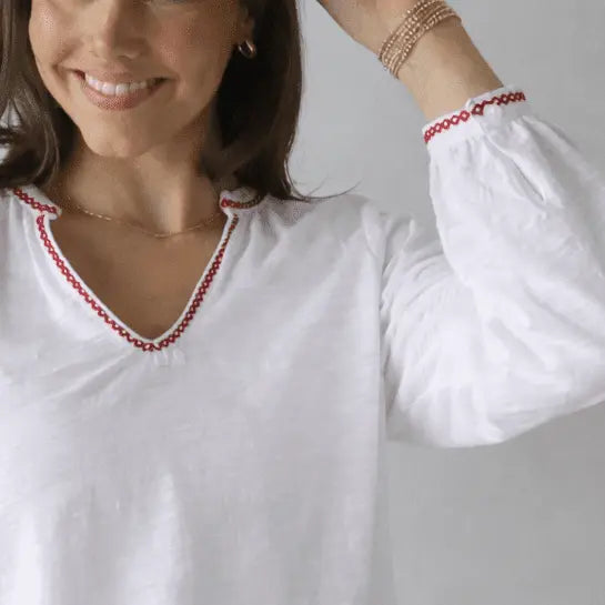 White women's long sleeve embroidered top by erin gray with red stitch and daisy design.