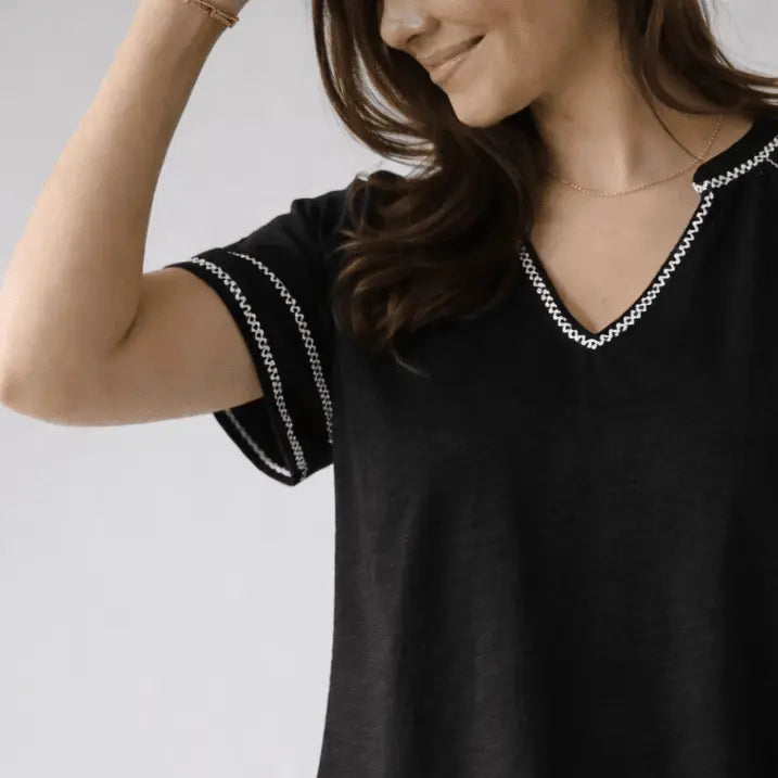 Black short sleeve embroidered top by erin gray with white stitch detailing, featuring a daisy pattern on the fabric.