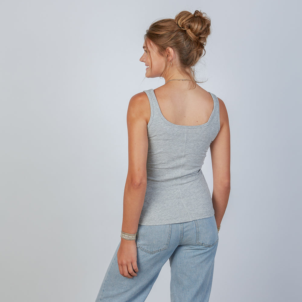 Woman wearing an erin gray light gray double layer tank top and jeans against a plain background