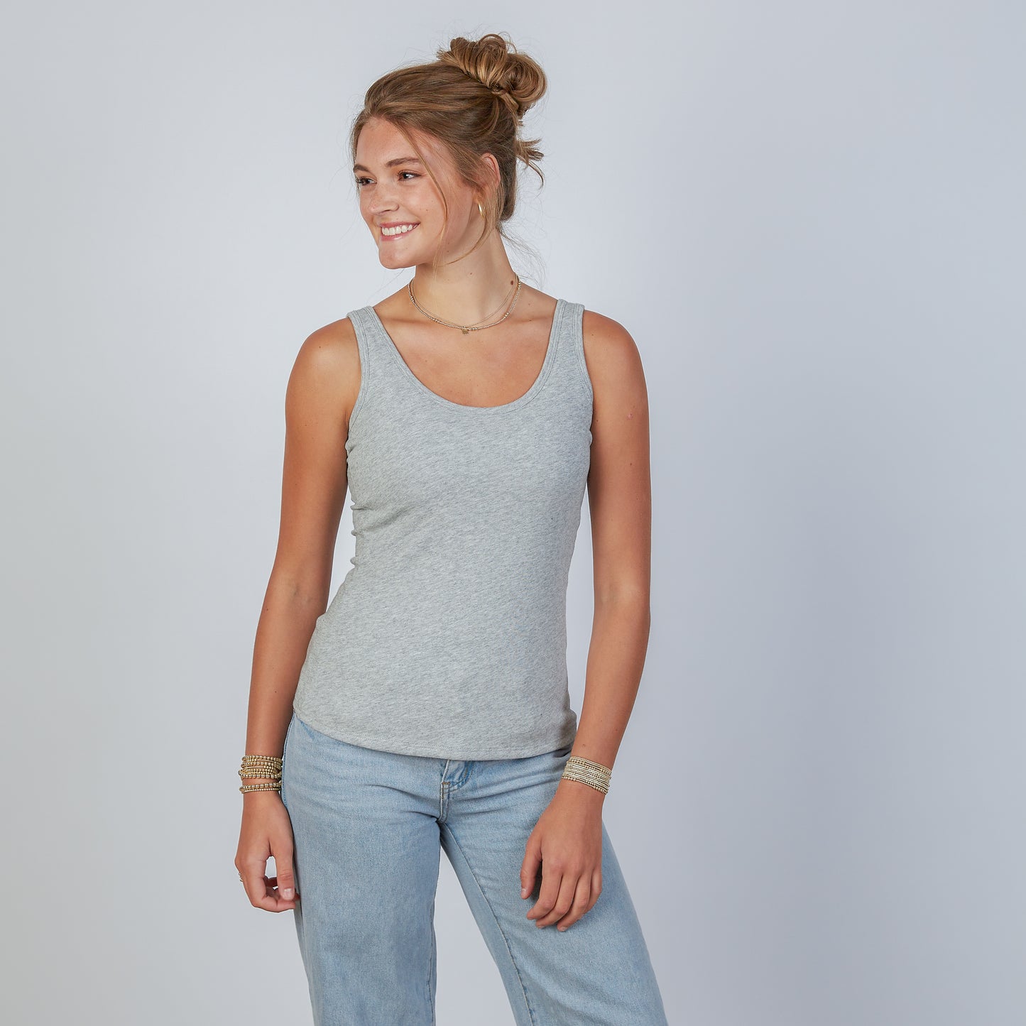 Woman wearing an erin gray light gray double layer tank top and jeans against a plain background
