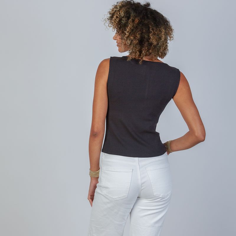 Woman wearing an erin gray design Havana black sleeveless top and white jeans against a gray background