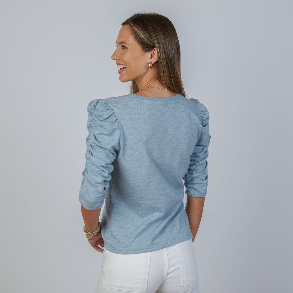 
                      
                        Woman wearing an erin gray design sophie dusty blue shirt and white jeans against a gray background
                      
                    